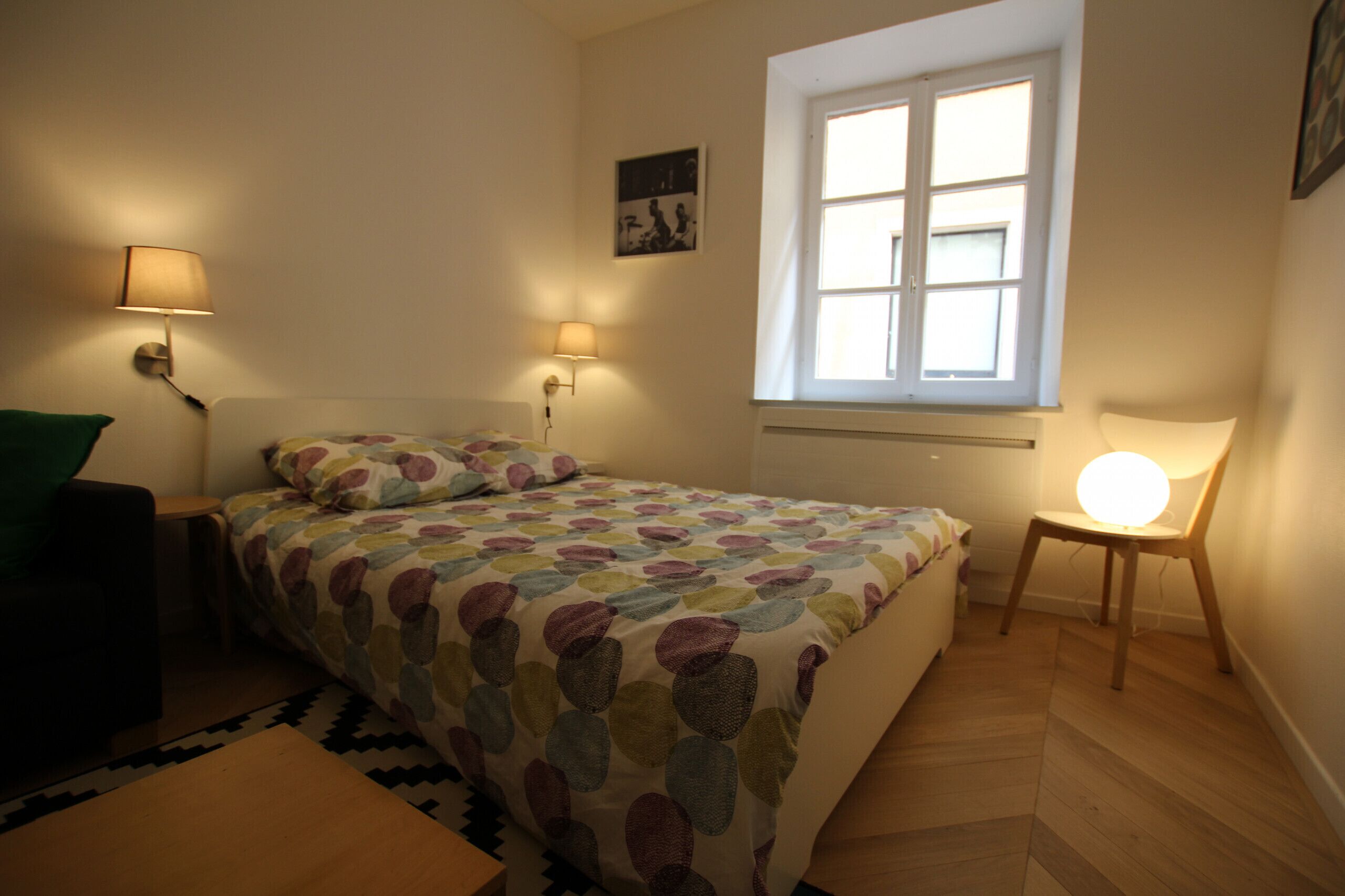 Et soveværelse med en seng, to sengeborde med lamper, et vindue og en stol.