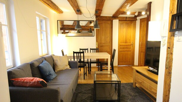 A living room with a sofa, coffee table, and TV. There is a dining area with a table and chairs. - Colmar Historic Center - Appartement PETITE VENISE 2 - BookingAlsace (Colmar)