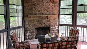 A stone fireplace with a decorative metal piece above it, surrounded by large windows and furnished with striped chairs. - Luxury Home Big Canoe Near Main Gate (Jasper)