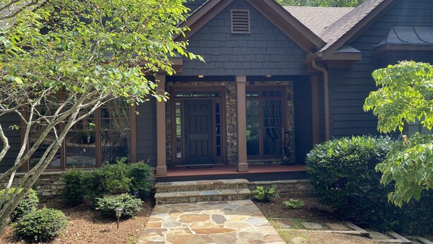 A house with a stone pathway leading to a wooden front door, surrounded by greenery and a stone wall. - Luxury Home Big Canoe Near Main Gate (Jasper)