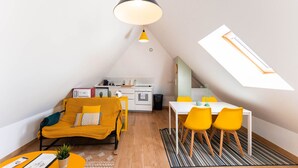 A compact living space with a kitchenette, a dining area with yellow chairs, a sofa with a yellow throw, and a skylight.
