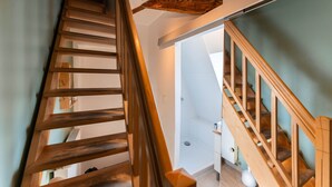 A wooden staircase with a modern design, leading to a room with a white radiator and a light-colored floor.