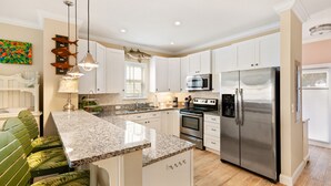 Una cocina moderna con gabinetes blancos, encimeras de granito, electrodomésticos de acero inoxidable y un banco verde.
