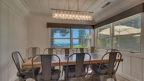 A dining area with a large wooden table and six chairs, a chandelier, and large windows with a view of the outdoors. - Belleview's Beauty - Lakefront - TLUXP (Homewood)