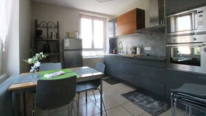 A modern kitchen with a dining area, featuring stainless steel appliances, a dining table with chairs, and a window providing natural light. - Colmar Centre Historique - Apartment Duplex MARIGNY - BookingAlsace (Colmar)