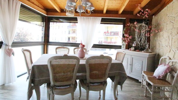 A dining area with a wooden ceiling, a chandelier, wicker chairs, a table with a white tablecloth, and a view of buildings through large windows. - Colmar Centre Historique - Apartment Duplex MARIGNY - BookingAlsace (Colmar)