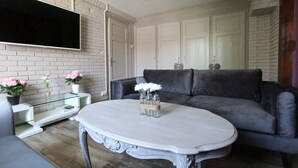 A living room with a grey sofa, a white coffee table, and a flat-screen TV mounted on a brick wall. - Colmar Centre Historique - Apartment Duplex MARIGNY - BookingAlsace (Colmar)