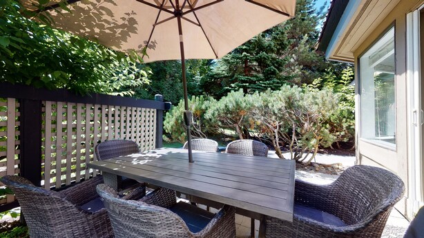 An outdoor patio with a wooden table and wicker chairs, a beige umbrella, and a wooden fence. - Lovely, 2 bedroom / 2 bathroom, Villas Foxglove townhome short walk to the slope (Whistler)