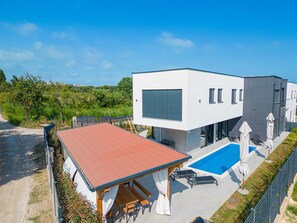 A modern two-story house with a swimming pool, outdoor seating, and a red-roofed patio.