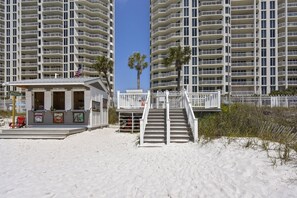 A beachside building with a small kiosk, a staircase leading to a balcony, and a palm tree. - 🌊Ground Floor | Beach Front | Upscale + Disc. Beach Service-Beach Blessing🌊 (Destin)