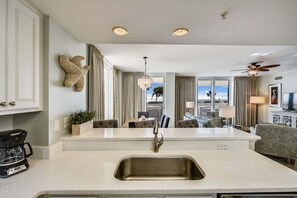 A modern kitchen with a central island, a dining area with a view, and a living room with a ceiling fan. - 🌊Ground Floor | Beach Front | Upscale + Disc. Beach Service-Beach Blessing🌊 (Destin)