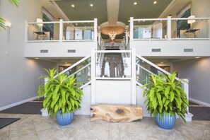 Interior espaçoso com escadaria central, duas grandes plantas em vasos e um candelabro.