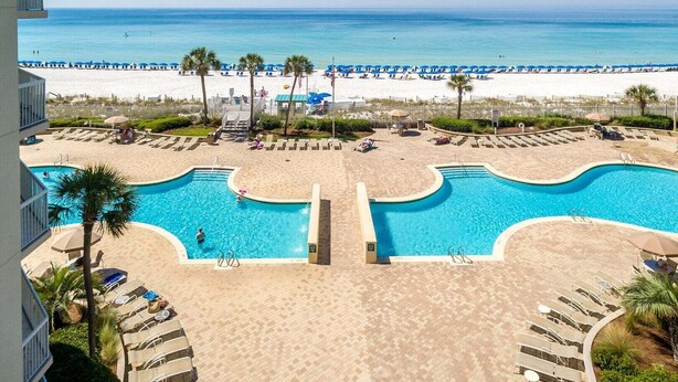 Un área de piscina con dos piscinas, una playa y vistas al océano.