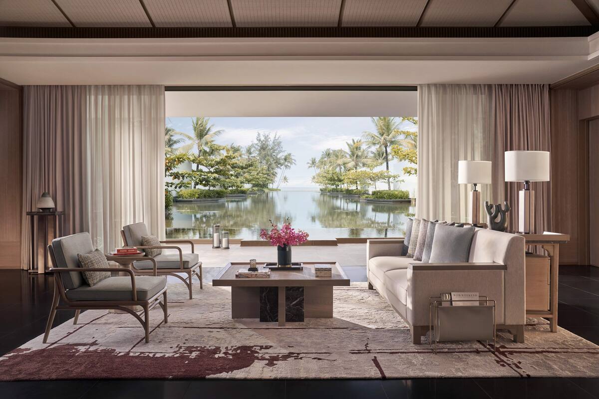 A modern living room with a view of a lake, featuring a sofa, chairs, a coffee table, and lamps.