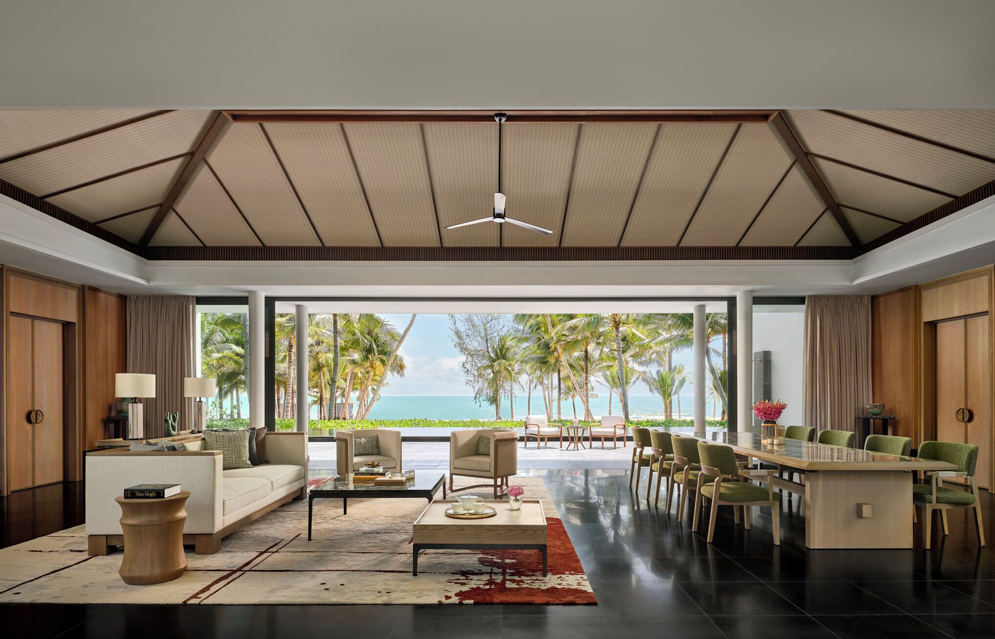 A modern living room with a large glass door leading to a balcony with a view of the ocean and palm trees.