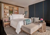 A modern bedroom with a large bed, bedside tables, a small side table, and a decorative wall unit.