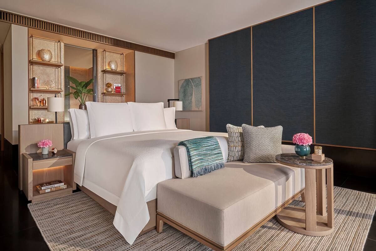 A modern bedroom with a large bed, bedside tables, a small side table, and a decorative wall unit.