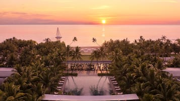 Relax by the serene pool surrounded by lush palm trees, overlooking the calm sea.
