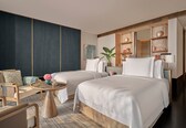 A hotel room with two beds, a sitting area with a chair and a small table, and a large mirror above the bed.