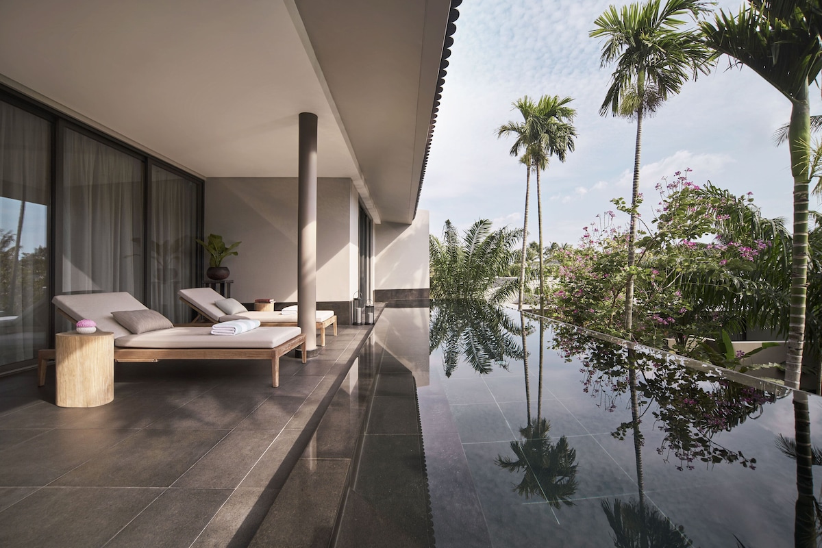 Zona d'estar exterior moderna amb una piscina reflectant, seients còmodes i vistes a la vegetació tropical.