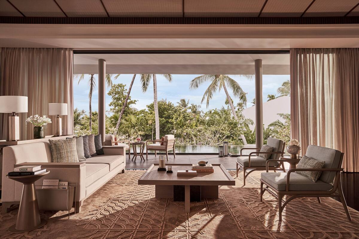 A modern living room with a sofa, armchairs, a coffee table, and a view of a pool and palm trees.