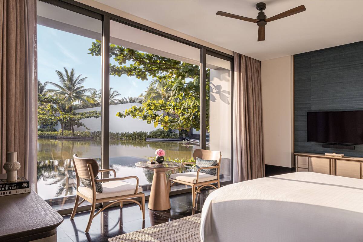 A hotel room with a large window, a bed, a TV, and a small table with chairs.