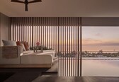 A modern living room with a sofa, pillows, a small table with a vase, and a view of the ocean at sunset.