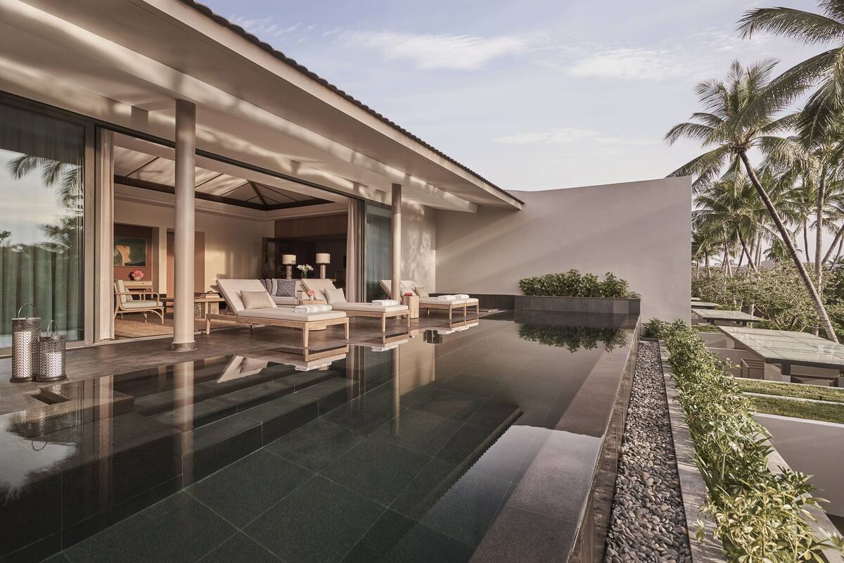 A modern resort with a pool, sun loungers, and a view of palm trees.