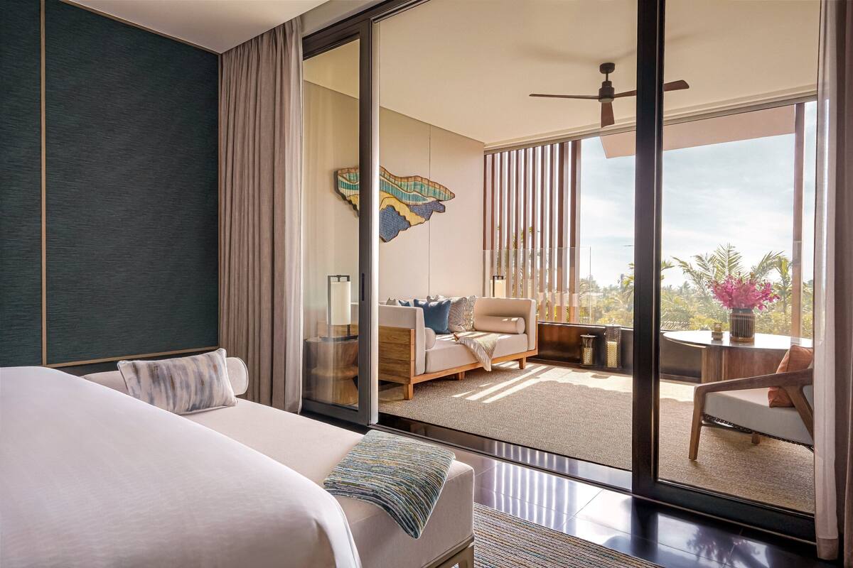 A modern hotel room with a large bed, a sofa, a dining area, and a balcony with a view.