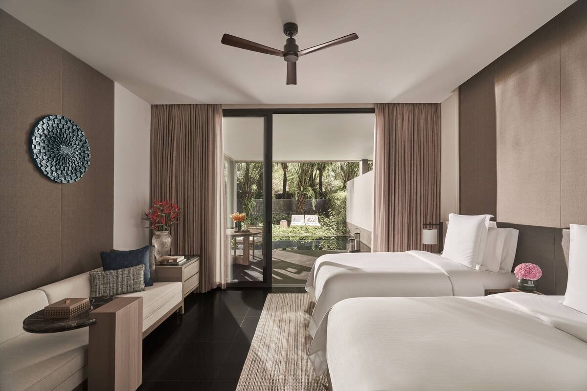 A modern hotel room with a bed, a sofa, a small table, and a ceiling fan.