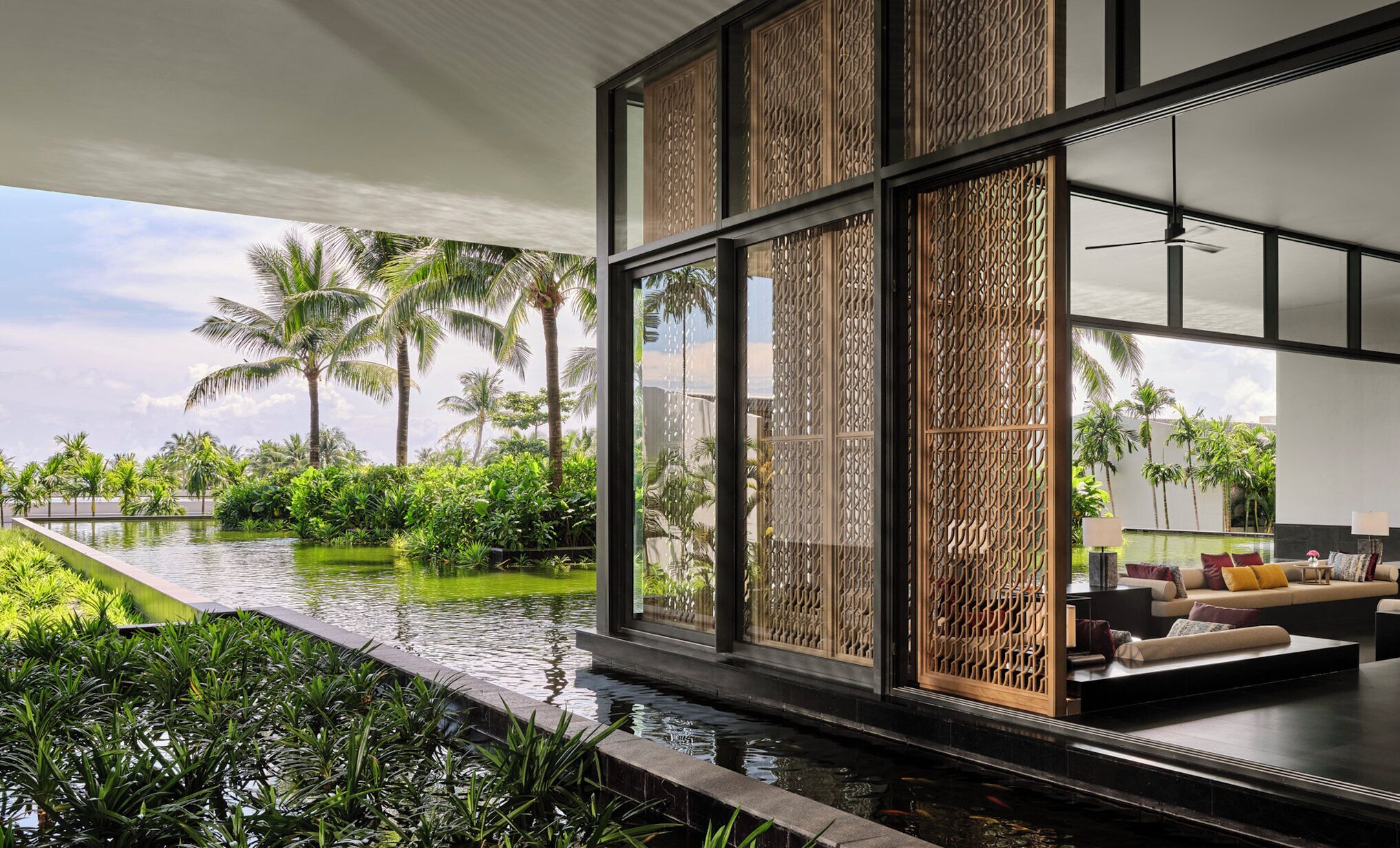 A modern interior with large windows overlooking a pool and tropical vegetation.