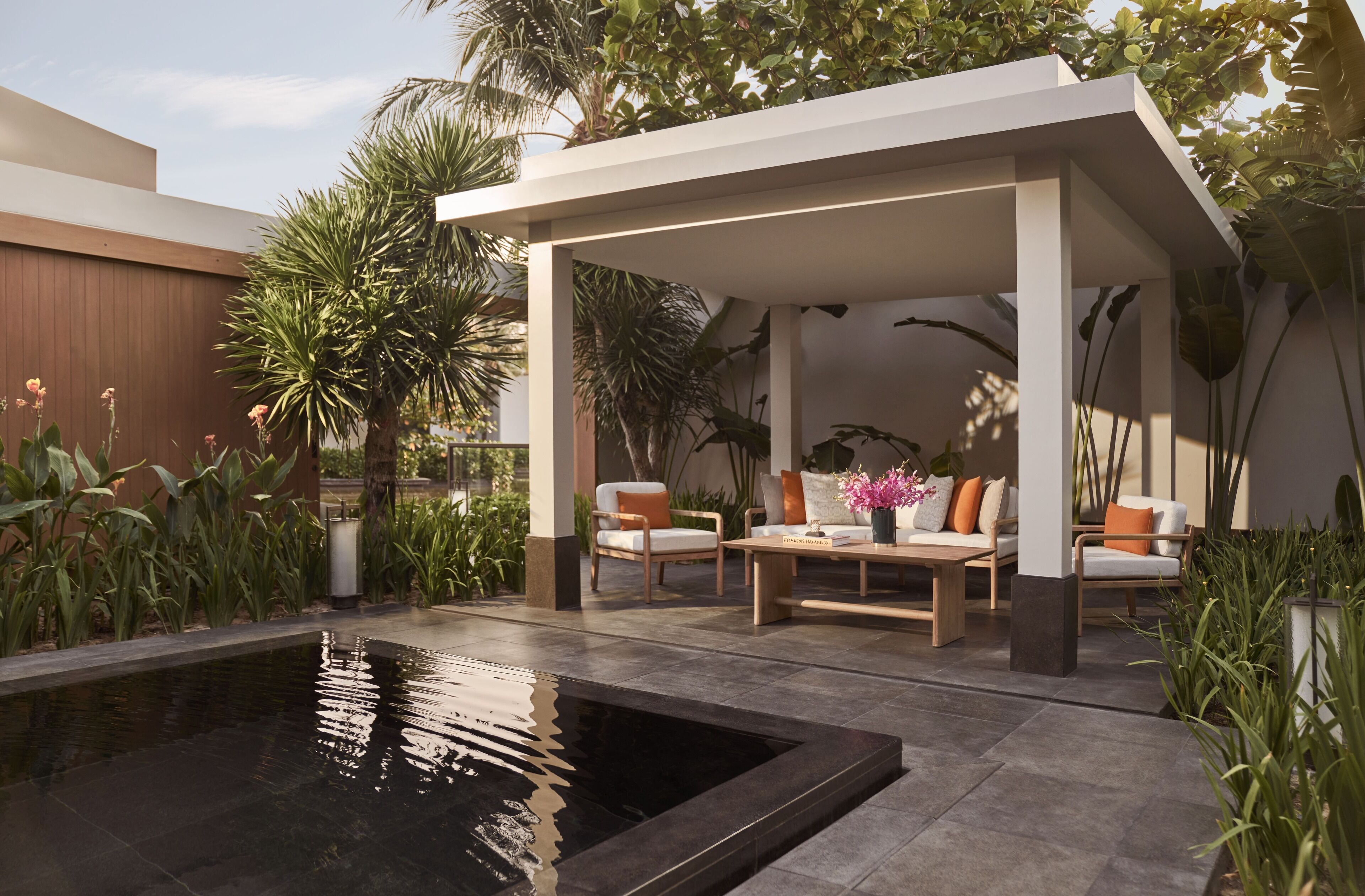 A modern outdoor patio with a pool, seating area, and lush greenery.