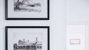 Two framed black and white photographs on a wall, one depicting a landscape with trees and a building, and the other showing a building with a porch. - The Loft (Castlemaine)