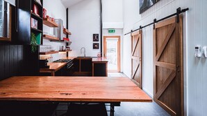 A modern kitchen with a wooden table, shelves with kitchenware, and a large wooden door. - Union Street (Castlemaine)