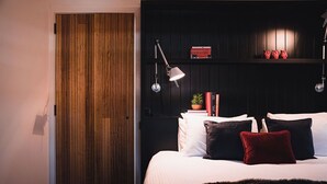 A bedroom with a wooden door, a bed with white and dark pillows, a red pillow, a small plant, and two books on a nightstand. - Union Street (Castlemaine)