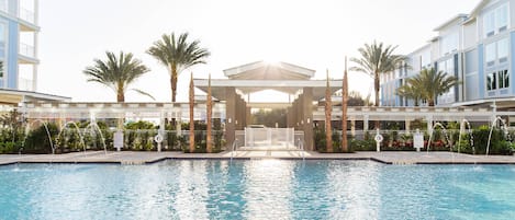 A swimming pool with a covered area, palm trees, and modern buildings in the background.