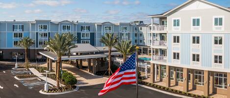 A multi-story hotel with a blue and white exterior, a parking lot with marked spaces, and an American flag.