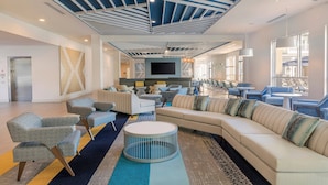 A modern hotel lobby with a large sectional sofa, armchairs, a flat-screen TV, and a ceiling with blue and white geometric patterns. - SpringHill Suites by Marriott Amelia Island (Fernandina Beach)