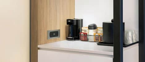 A modern kitchenette with a wooden panel design, a glass shelf, a coffee maker, and a coffee grinder.