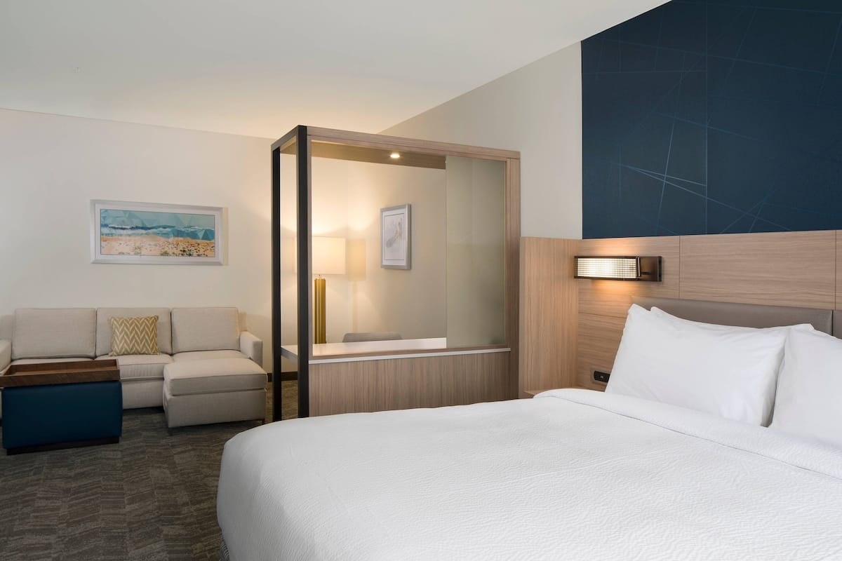 A hotel room with a large bed, a sofa, a small table, and a mirror.