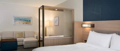 Habitación de hotel con una cama grande, un sofá, una mesita y un espejo.