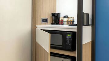 A compact kitchenette with a microwave, coffee maker, and storage cabinets.