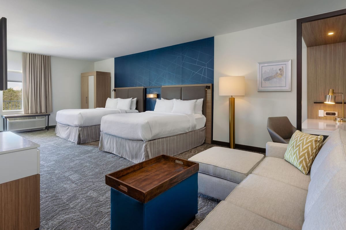 A hotel room with two beds, a sofa, a coffee table, a desk, and a large window with curtains.