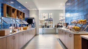 A modern hotel kitchen with wooden cabinets, a central island, and a view of the city through large windows.