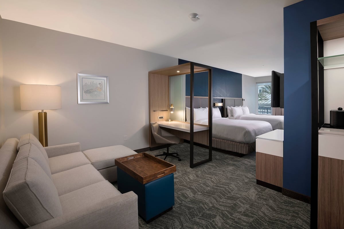 A hotel room with a sofa, a desk, a bed, a small table, and a mirror.