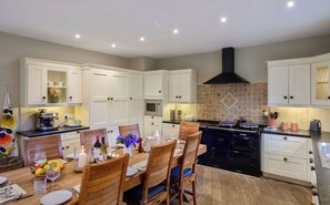 Une cuisine moderne avec des meubles blancs, une cuisinière noire et un coin repas comprenant des chaises en bois et une table dressée pour quatre personnes.