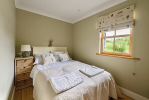 Une chambre à coucher comprenant un lit, une table de chevet, une lampe et une fenêtre donnant sur un paysage verdoyant.