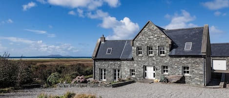 A stone house with a gravel driveway and a view of the countryside.