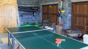 Une table de ping-pong dans une pièce avec un mur en pierre, une porte en bois et une chaise en métal.