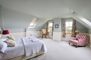 Ein Schlafzimmer mit einem großen Bett, einem Sessel, einem rot-weißen Schachstuhlsessel und einem Fenster mit Vorhängen.